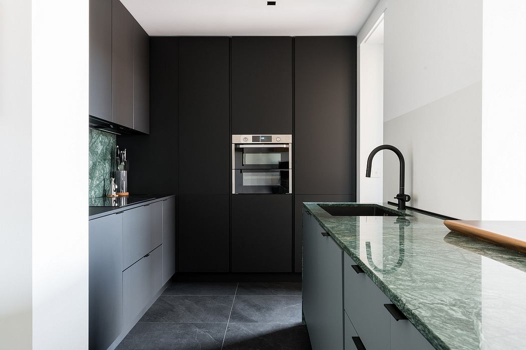 A modern kitchen design with black cabinets, marble countertops, and built-in appliances.