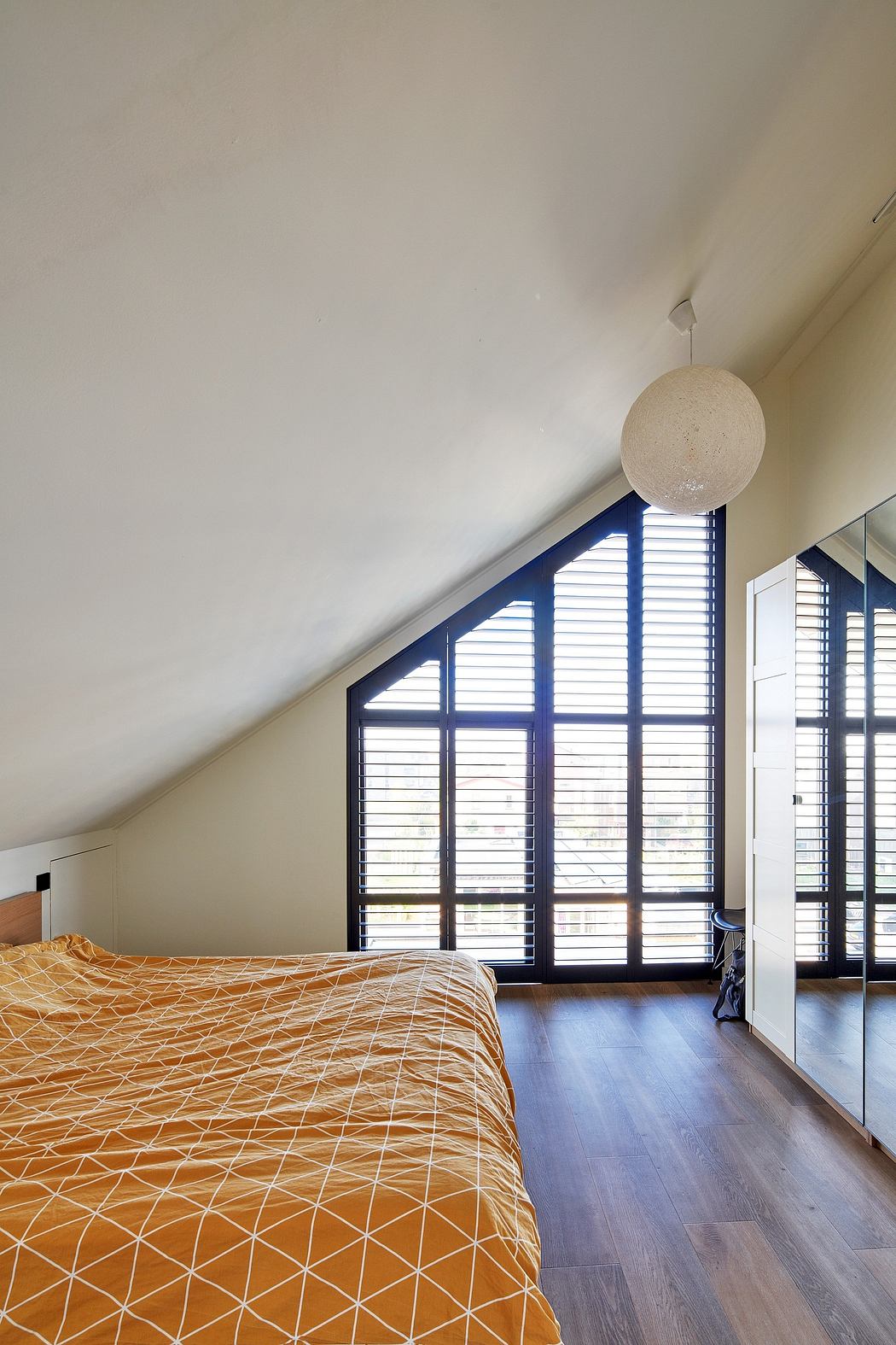 An interior space with angled windows, hardwood floors, and a patterned bedspread.