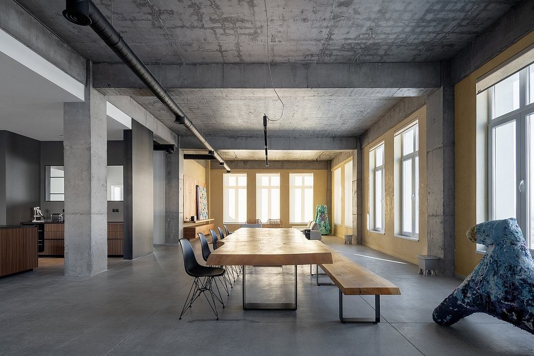 Spacious open-plan office with exposed concrete walls, wooden table, and modern chairs.