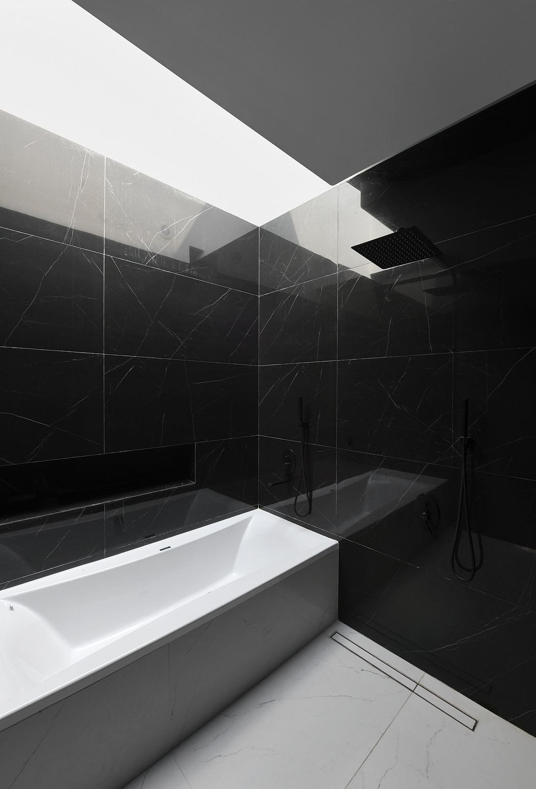 A modern, minimalist bathroom with black marble tiles, a white tub, and a sleek shower.