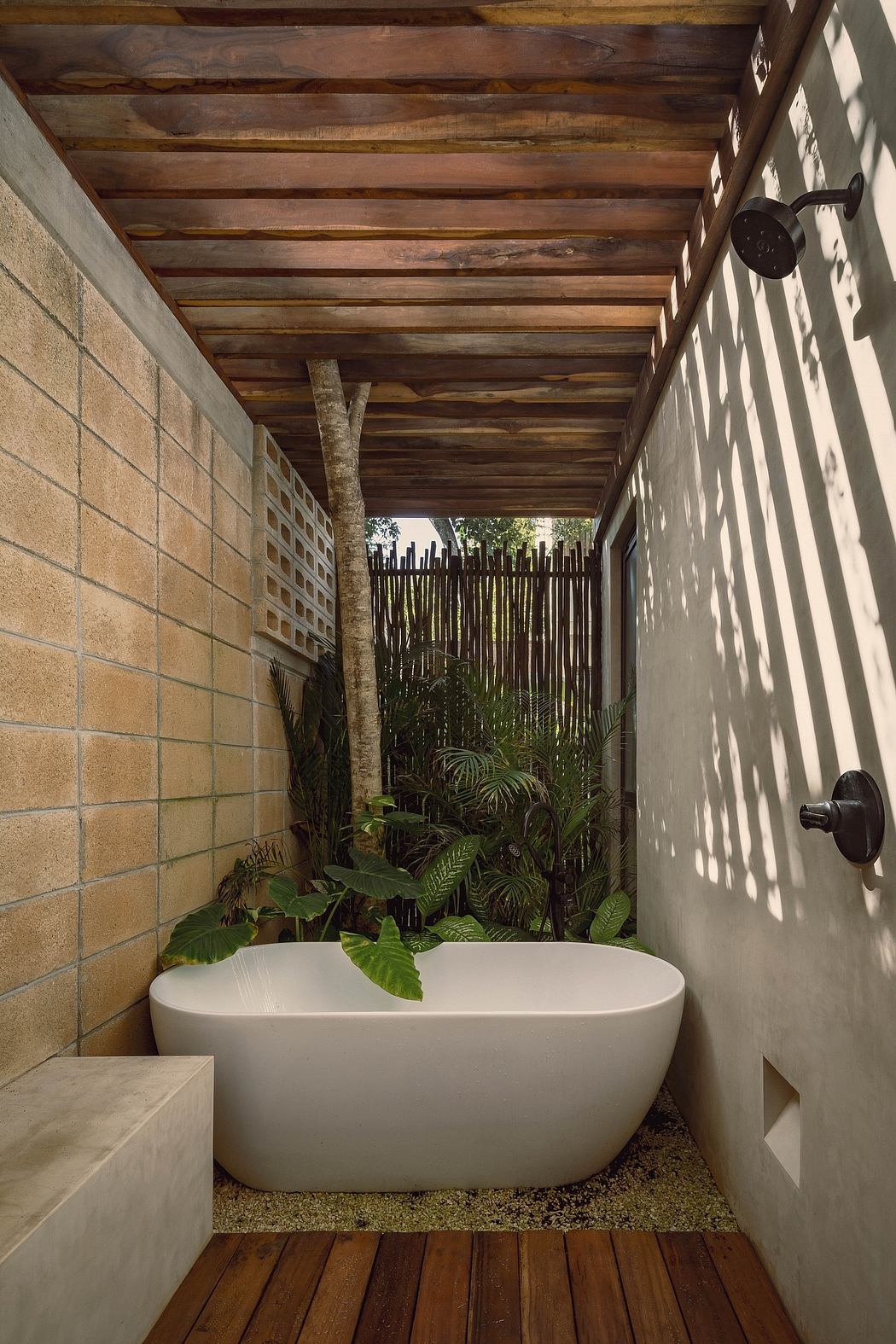 Rustic wooden ceiling, tropical plants, and an inviting freestanding bathtub create a serene outdoor bathroom.