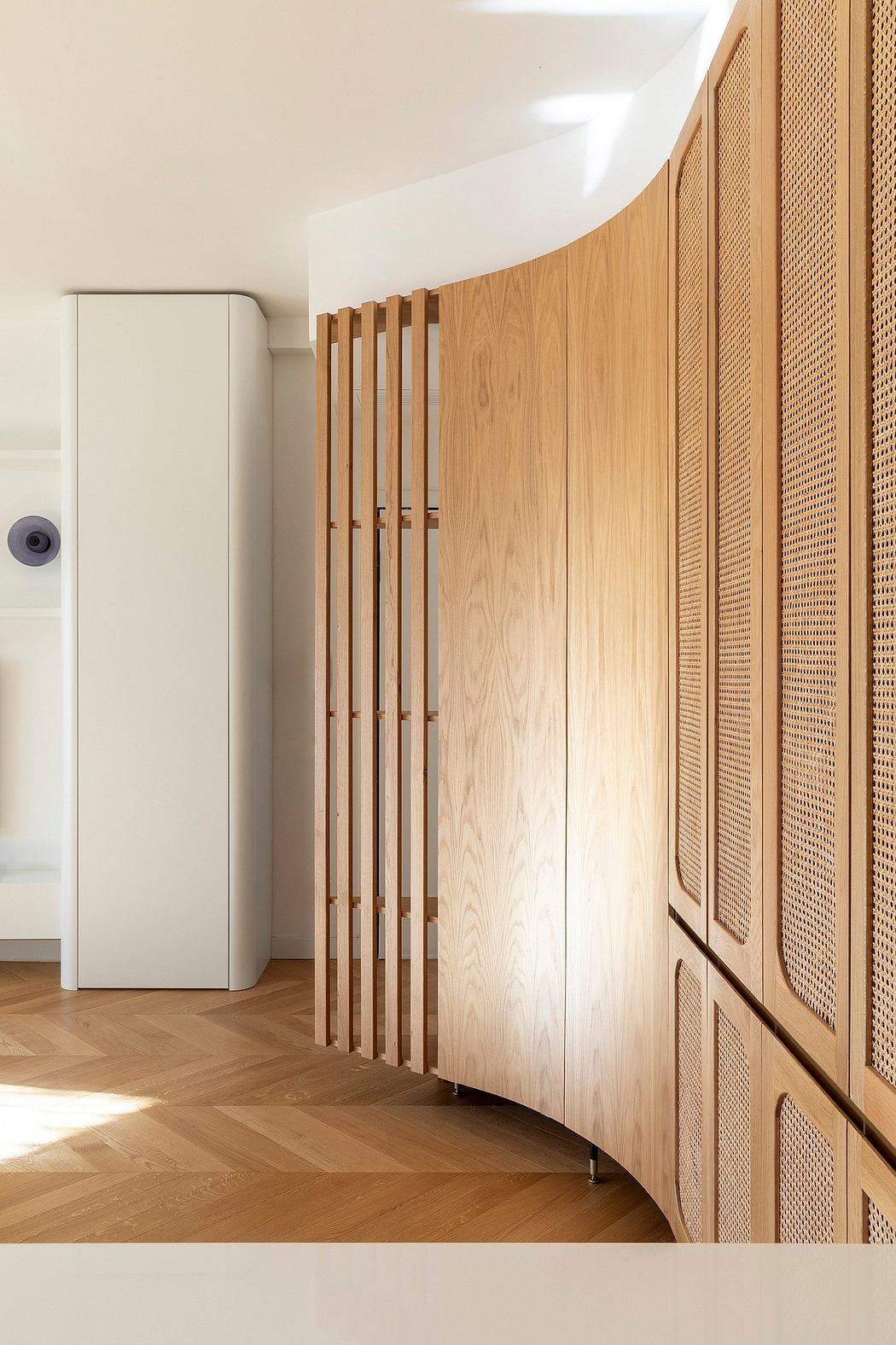 Curved wood paneling with vertical slats, contrasting with smooth white walls and herringbone floor.