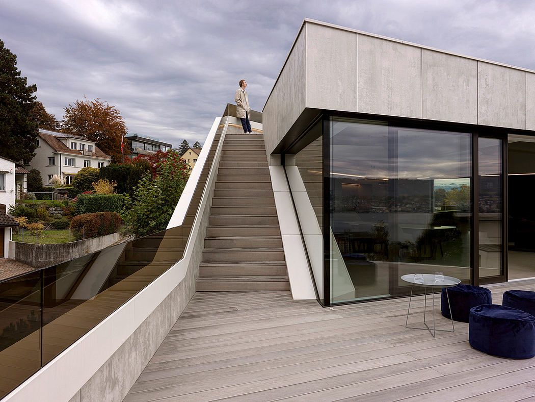Sleek modern home with concrete stairs, glass walls, and a wooden deck overlooking the landscape.