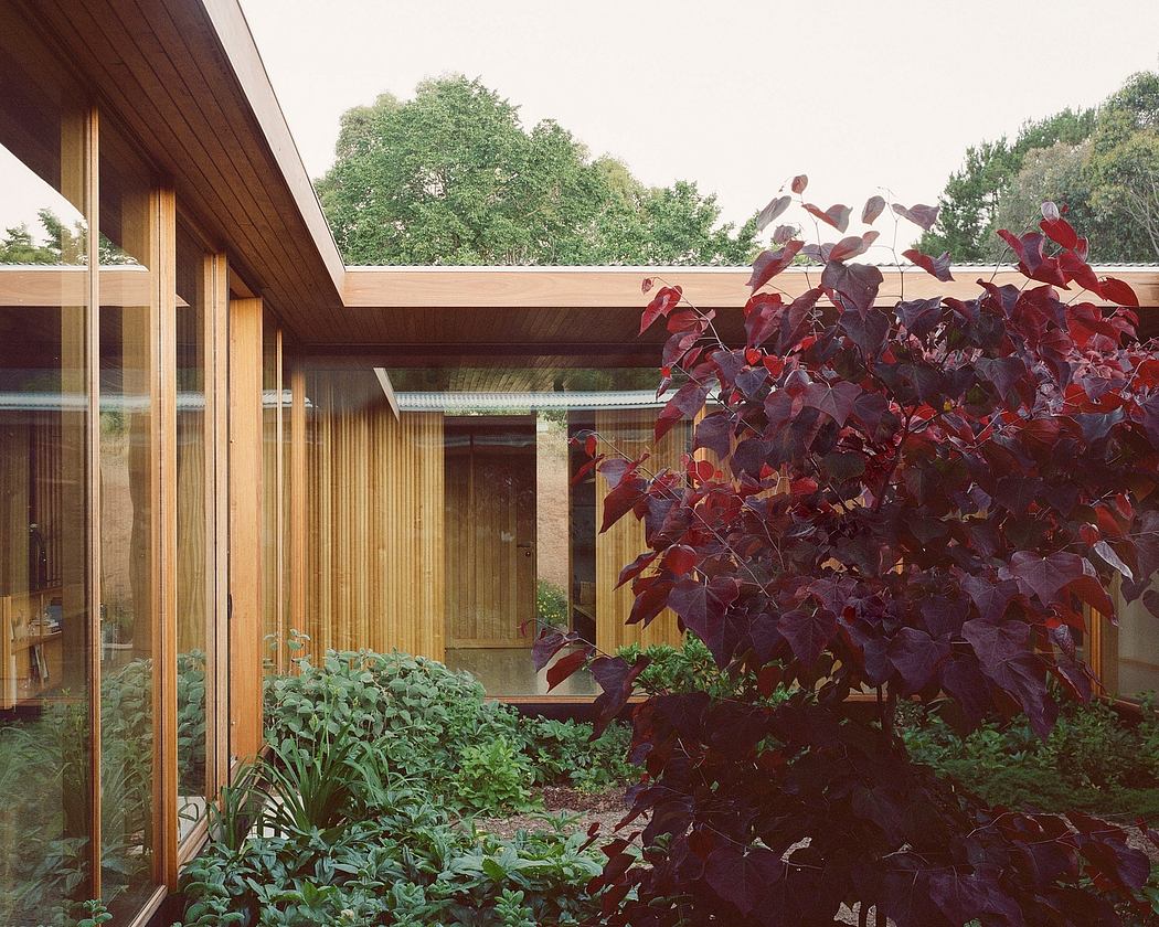 A wooden structure with large windows overlooking a lush garden with vibrant foliage.