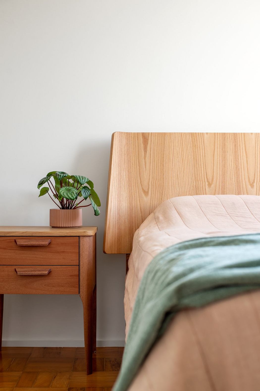 A cozy bedroom with a wooden headboard, nightstand, and a potted plant decor.