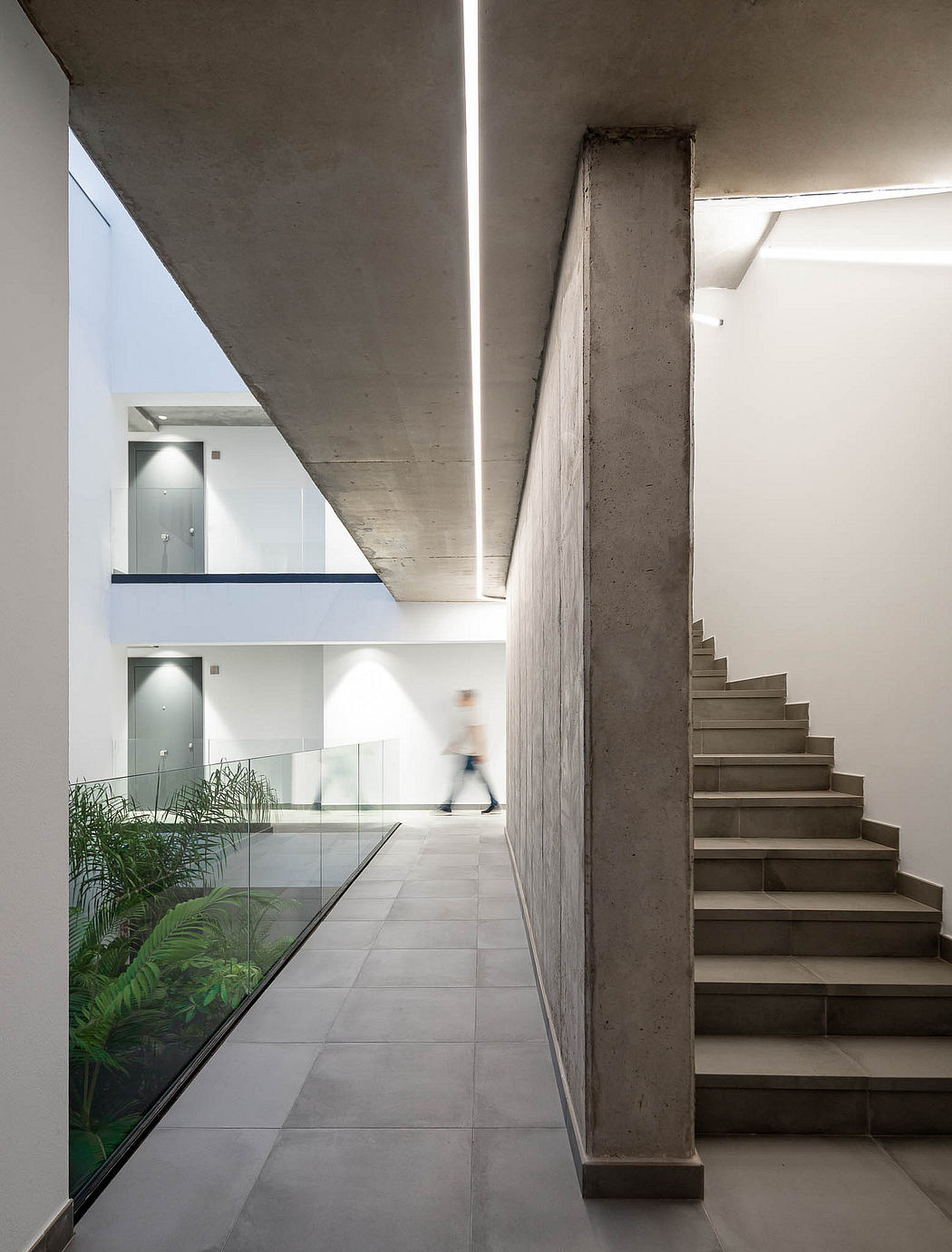 Minimalist interior with concrete walls, glass partitions, and a staircase leading to the upper level.