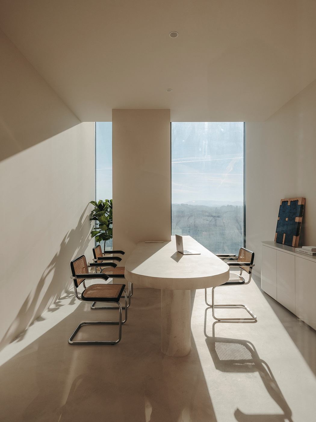 A modern minimalist office space with large windows overlooking a scenic view.
