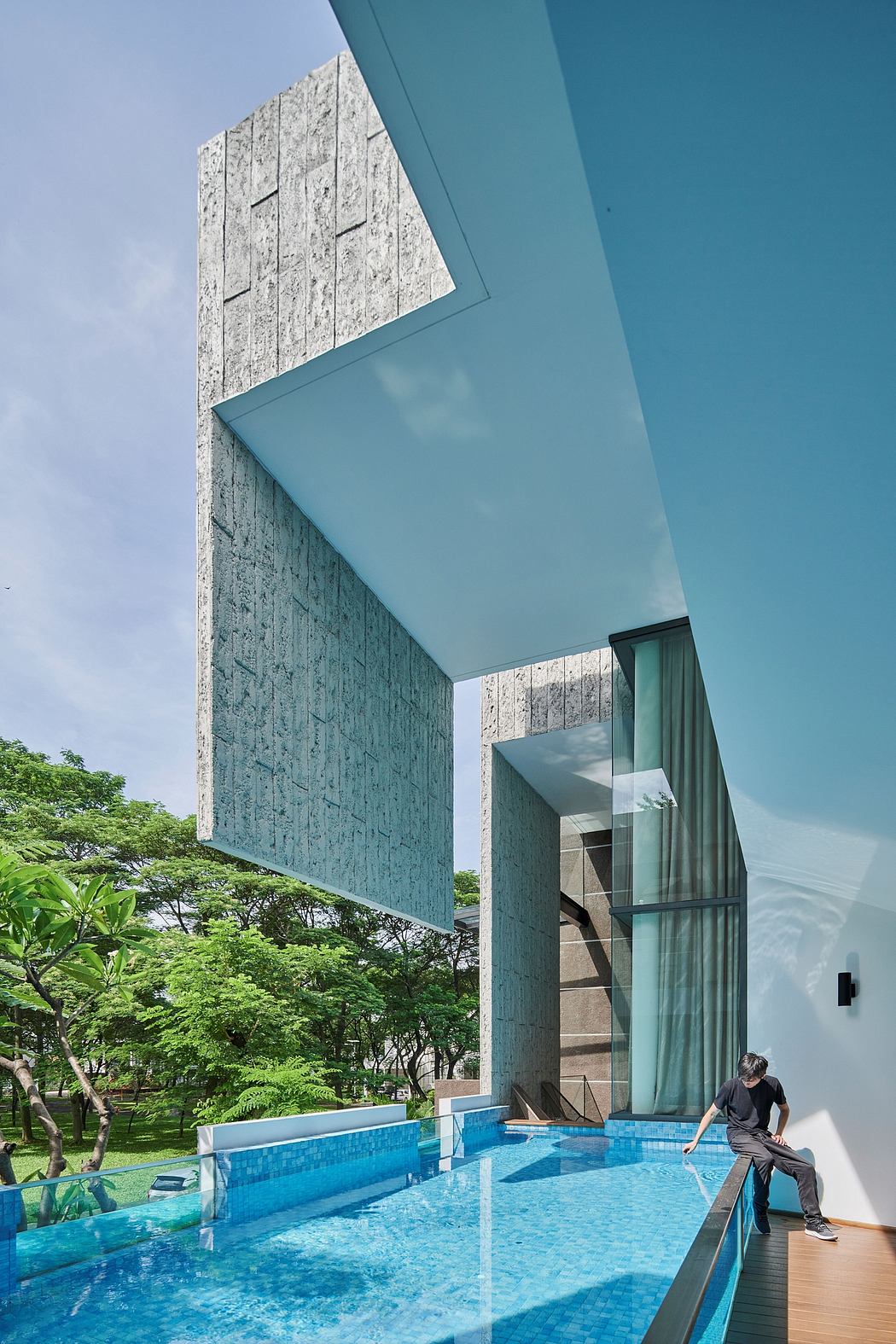 Modern architecture with textured walls, glass panels, and an inviting pool set in lush greenery.