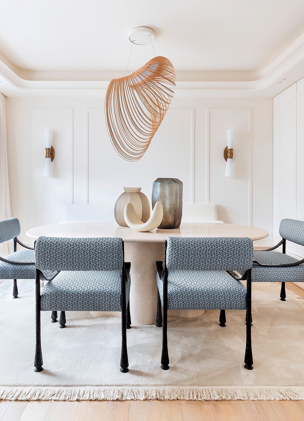 A modern and minimalist dining room featuring a sculptural light fixture, patterned chairs, and a stylish table with decorative vases.