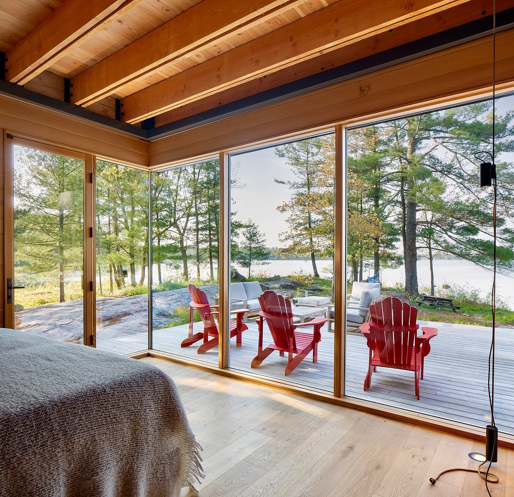 Cozy cabin interior with vaulted wood-beamed ceiling, lakeside deck, and red Adirondack chairs.