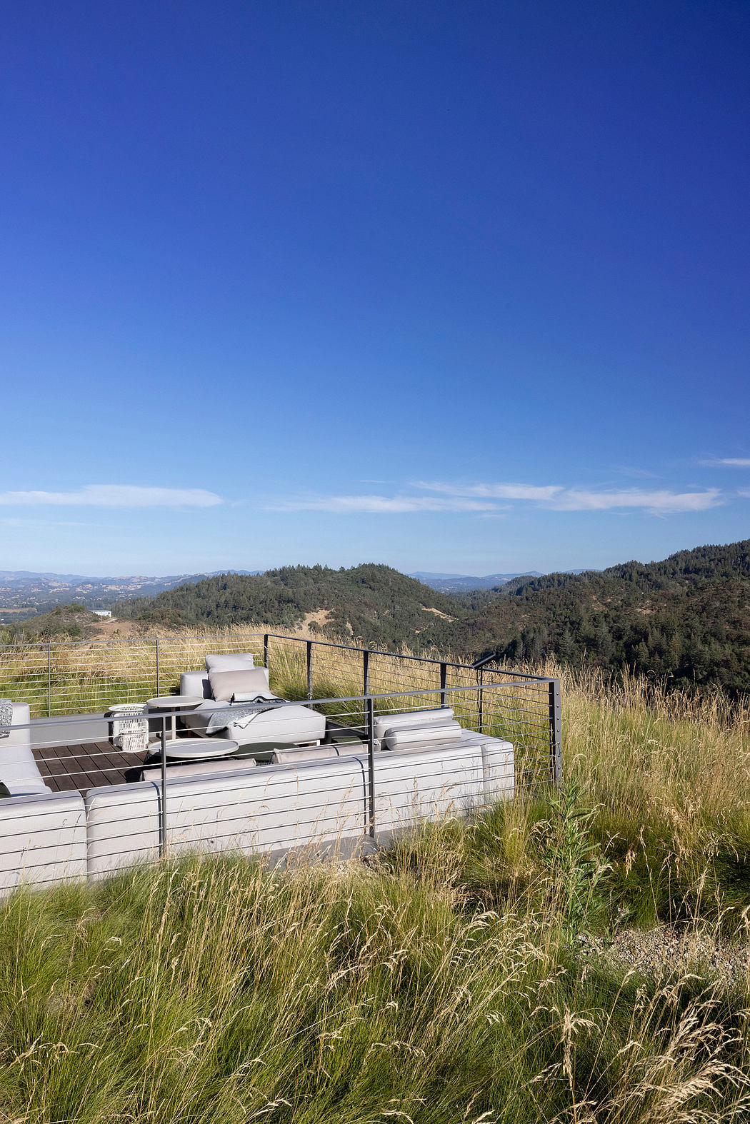A modern outdoor seating area overlooking a mountainous landscape, with wooden decking and metal railing.