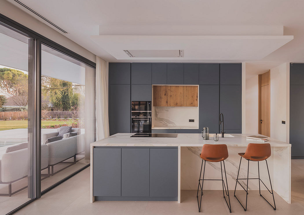 Modern kitchen with sleek gray cabinetry, wood accents, and large windows overlooking a garden.