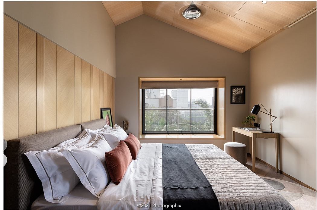 Cozy bedroom with warm wood paneling, large window, and minimalist decor.