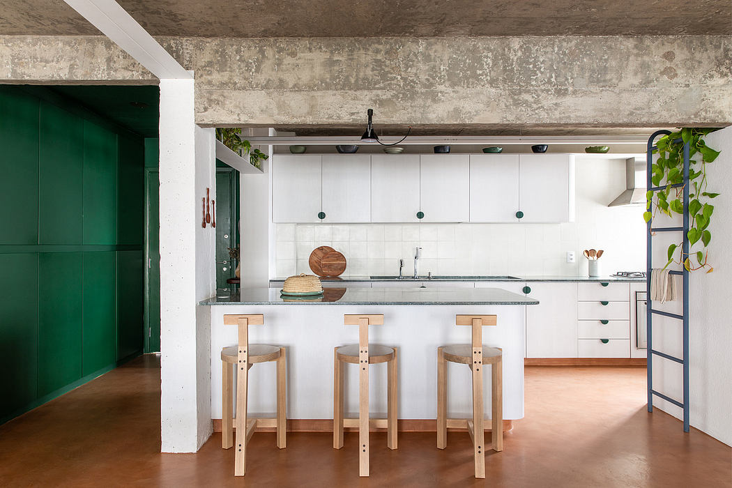 A modern, minimalist kitchen with concrete walls, white cabinets, and wooden barstools.