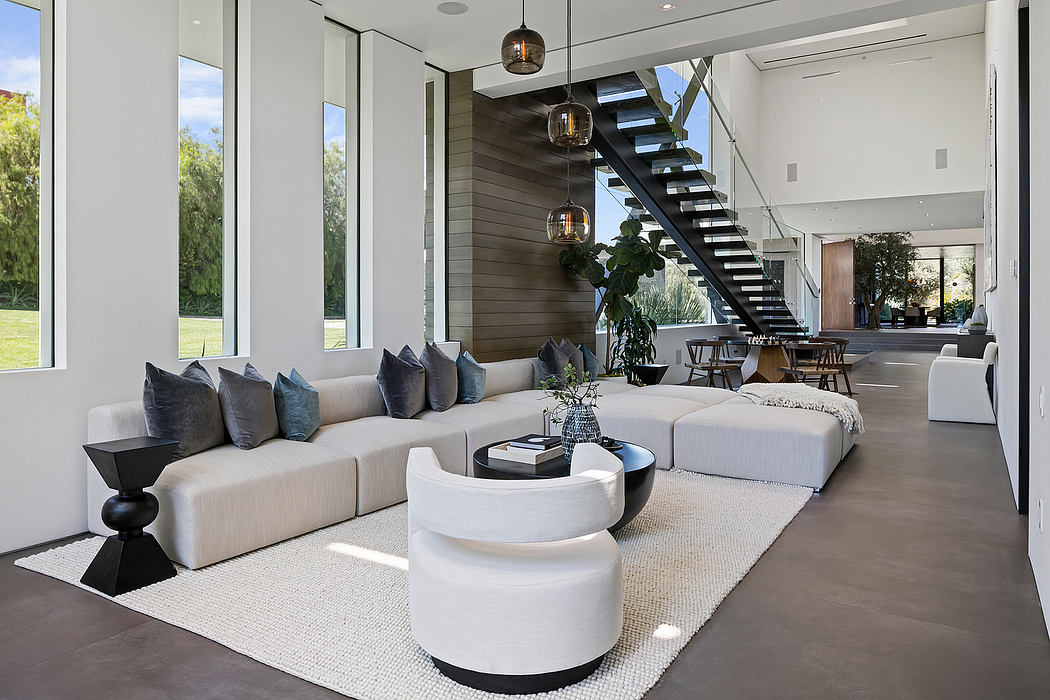 Modern, minimalist living room with large windows, sleek furniture, and a sculptural staircase.