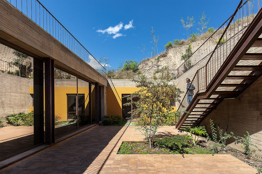 Modernist courtyard with stone walls, wooden stairs, and landscaped greenery.