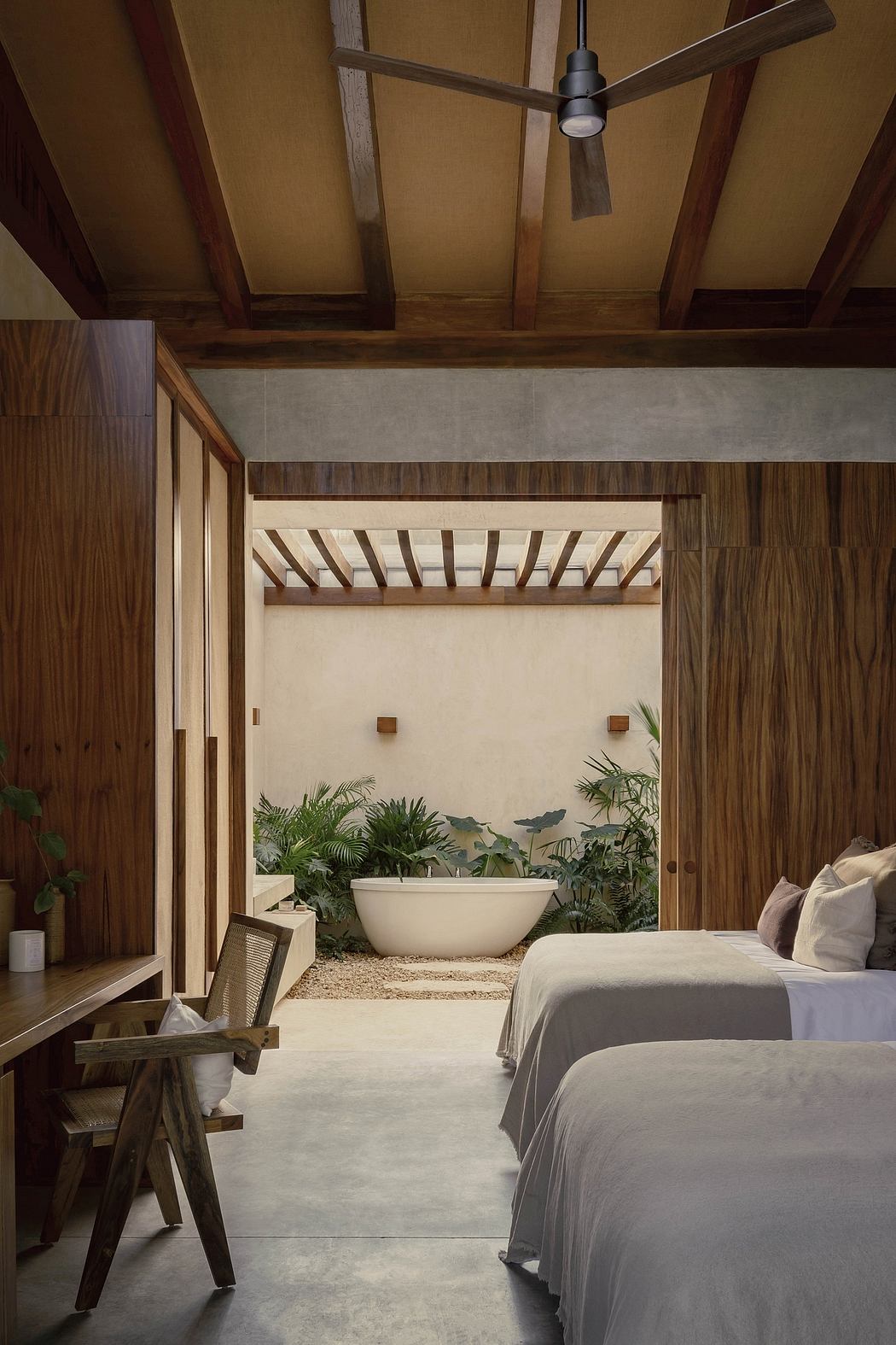 Rustic wooden beams, tropical plants, and a freestanding bathtub create a serene ambiance.
