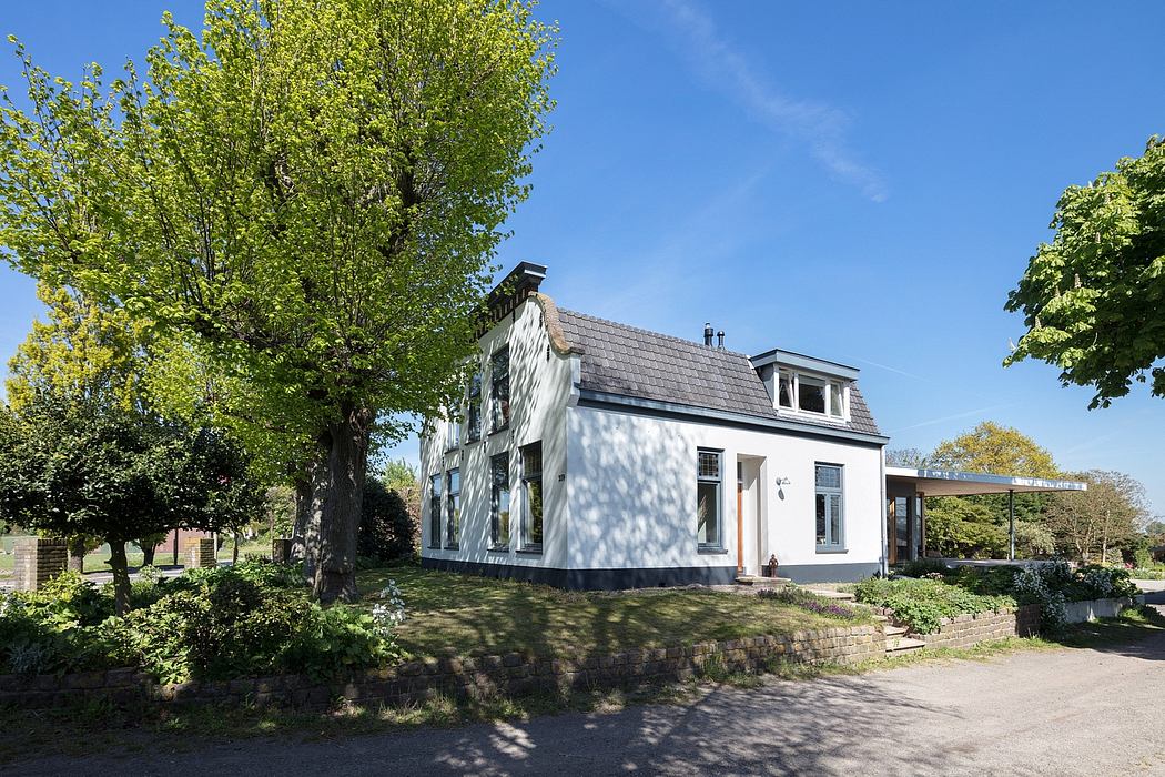 A white two-story house with a gabled roof and shuttered windows surrounded by lush trees.