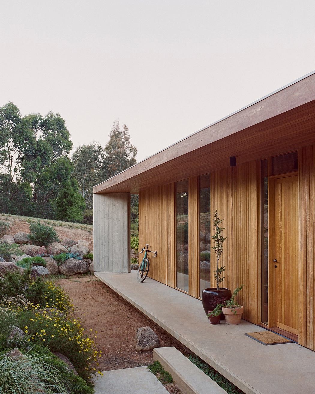 Wooden exterior of modern house surrounded by lush greenery and rocks.