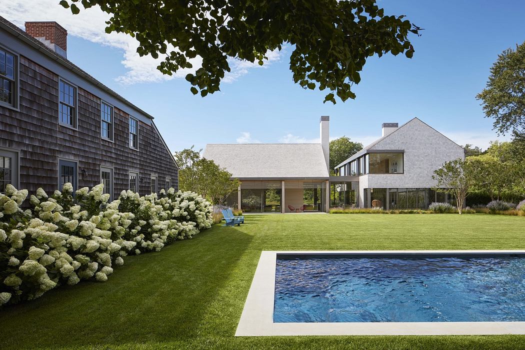 Spacious backyard with a pool, lush greenery, and a modern, shingle-style home.