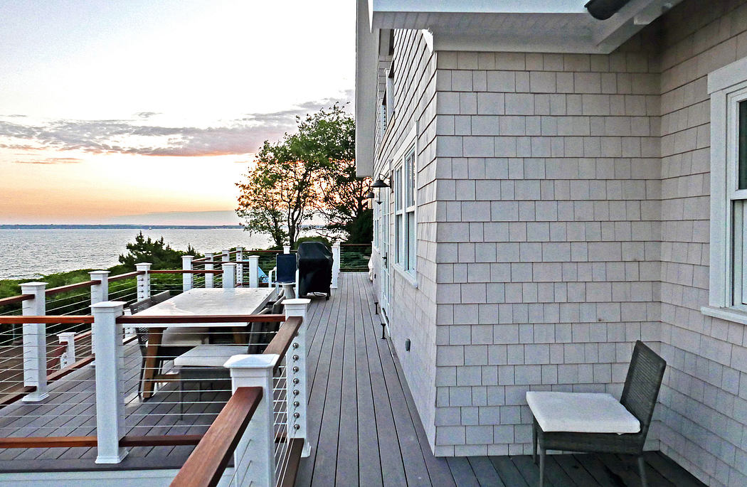 Outdoor wooden deck with stone-clad walls, patio furniture, and scenic waterfront view.