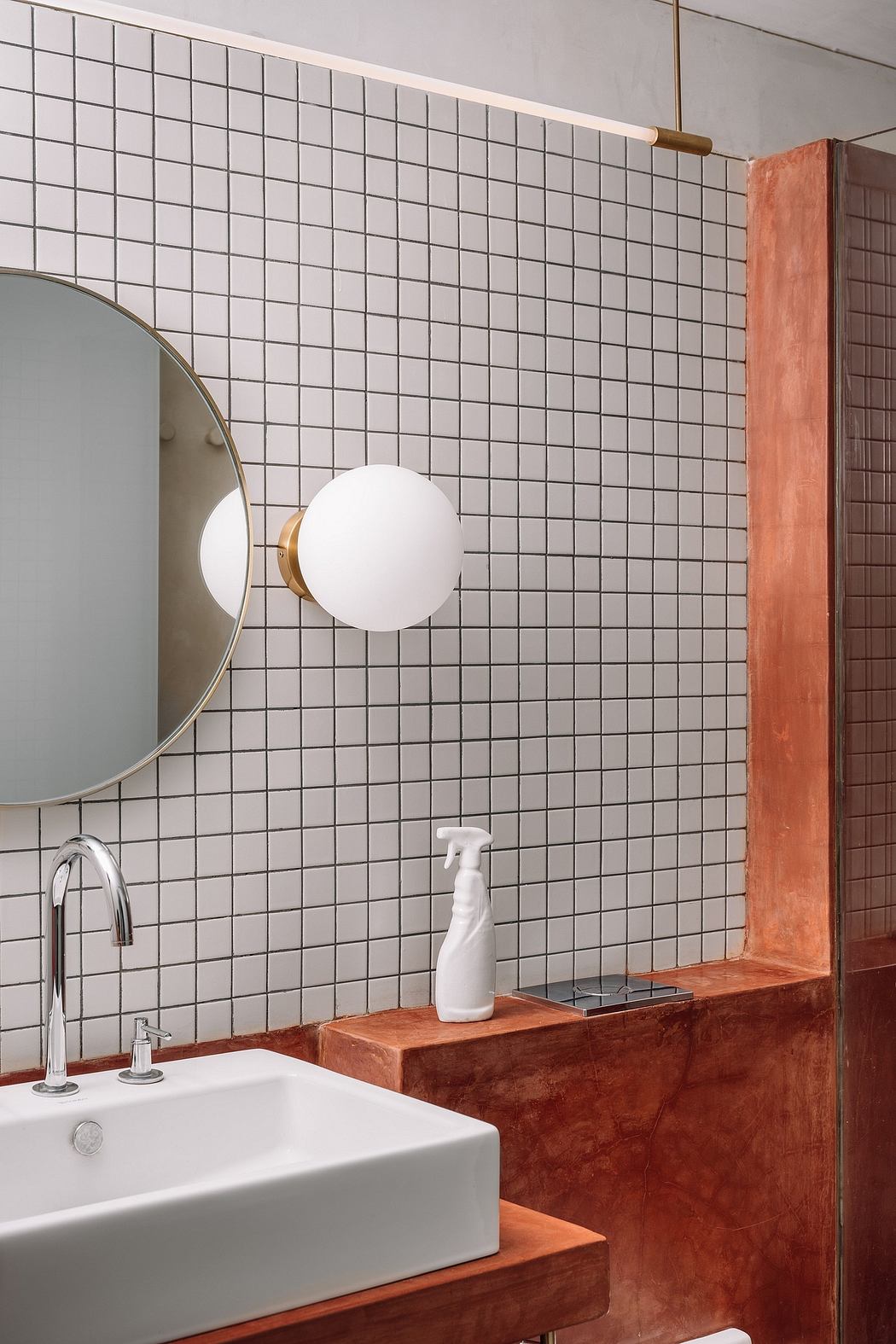 A modern bathroom with a tiled wall, a circular mirror, and a white sink on a wooden vanity.