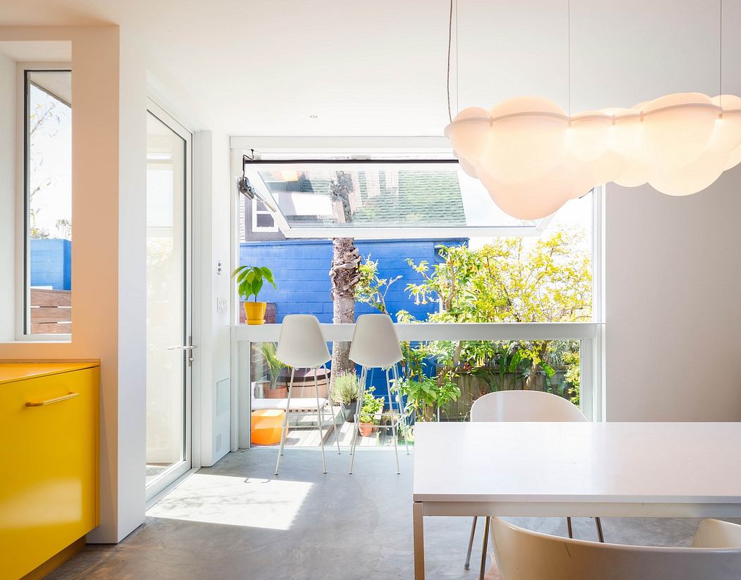 Bright, modern dining area with cloud-like lighting fixture, floor-to-ceiling windows, and lush greenery.