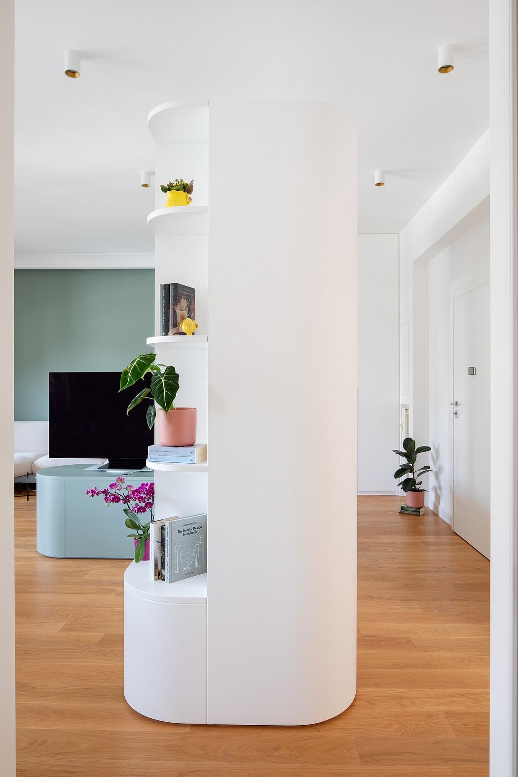 Modern, minimalist entryway with white shelving unit, potted plants, and hardwood floors.