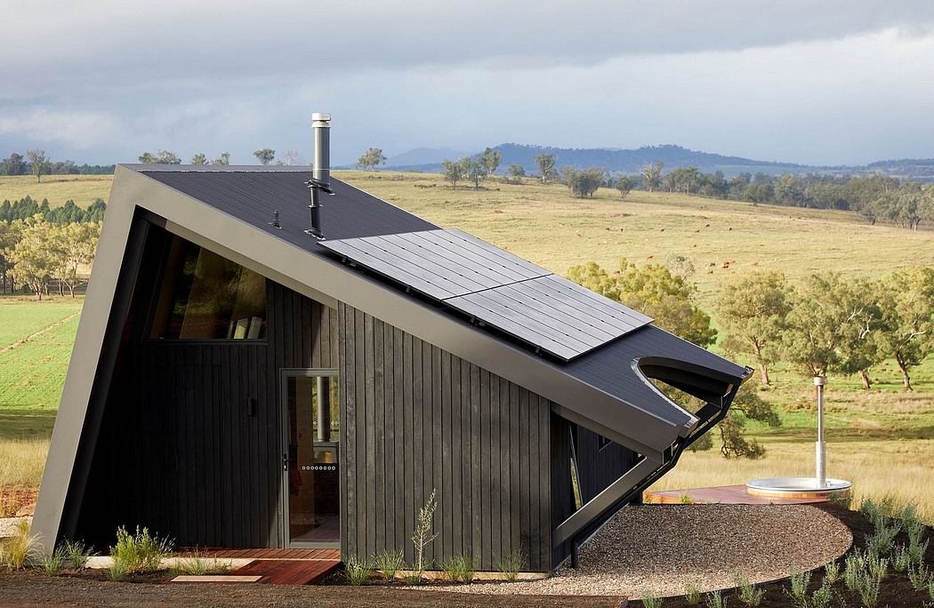A modern cabin-style home with a distinctive slanted roof and solar panels, surrounded by a rural landscape.