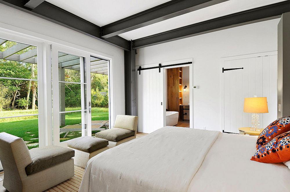 Spacious bedroom with floor-to-ceiling windows, wooden beams, and a sliding barn door.