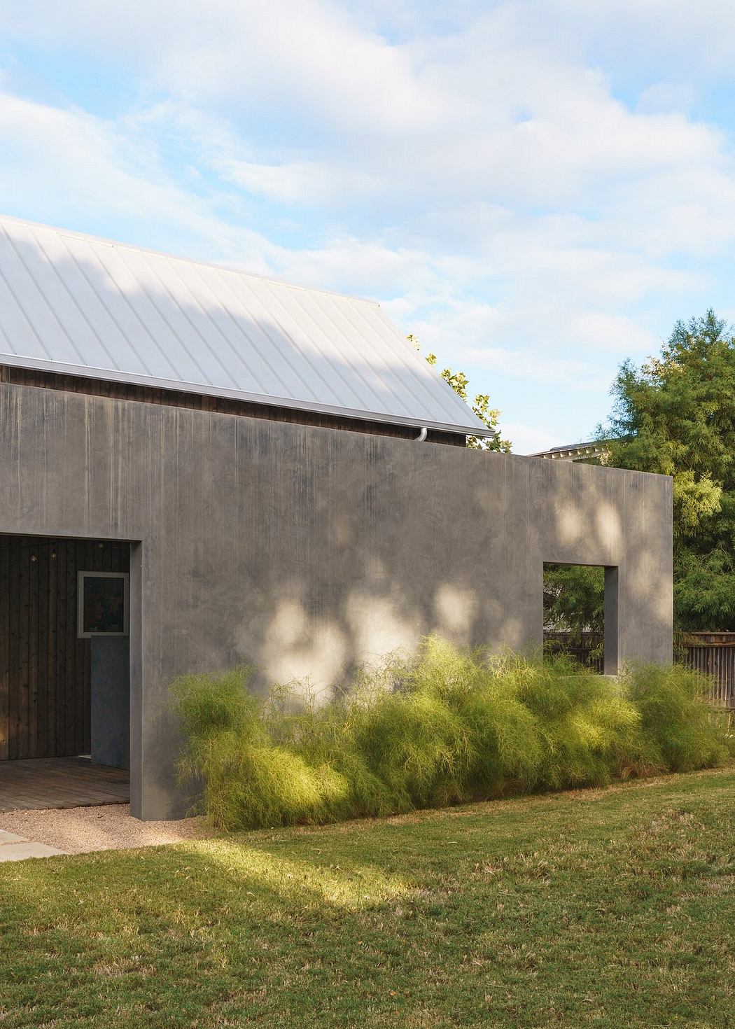 A modern, minimalist building with a metal roof, surrounded by lush greenery.