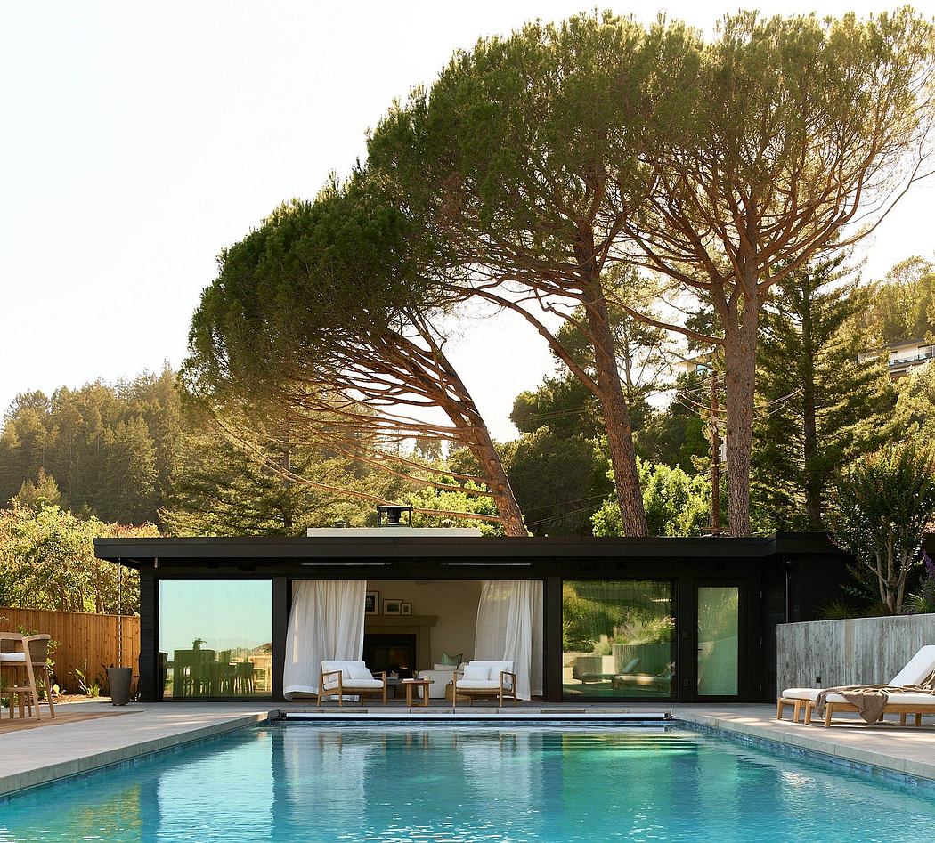 A modern poolside pavilion with glass walls and a slanted roof amid lush greenery.
