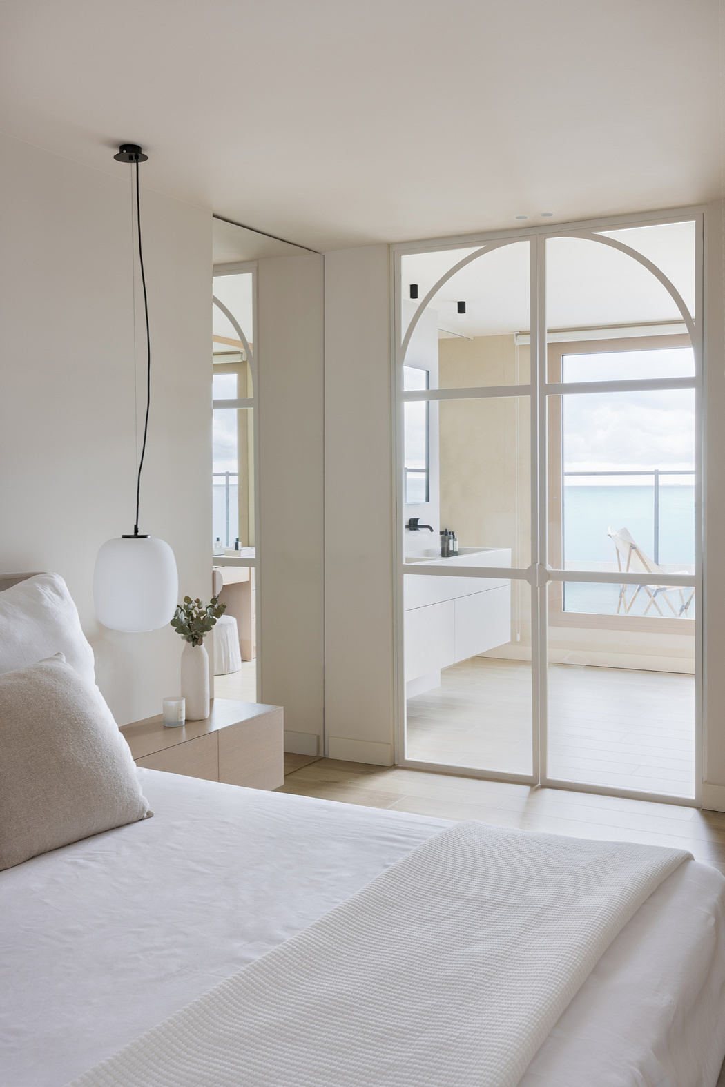 Bright, airy bedroom with arched windows, minimalist furnishings, and a view of the outdoors.