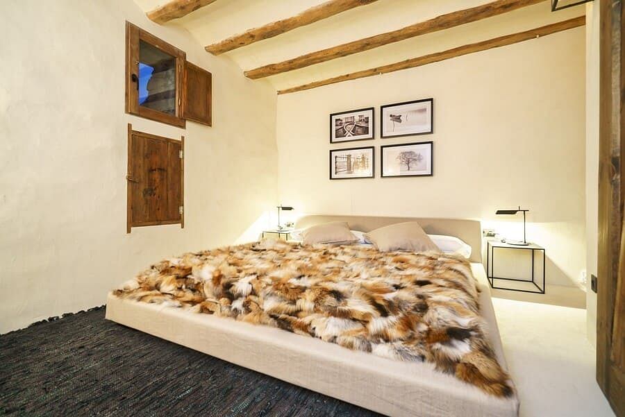 Rustic bedroom with exposed wooden beams, furry bedspread, and minimalist artwork.