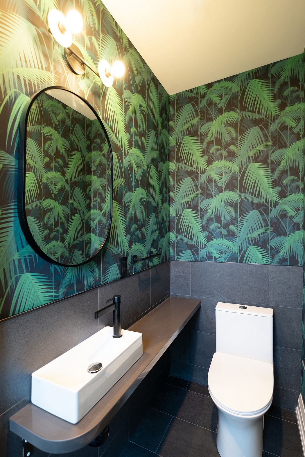 A modern bathroom design featuring a tropical palm leaf wallpaper, a floating vanity, and a round mirror.