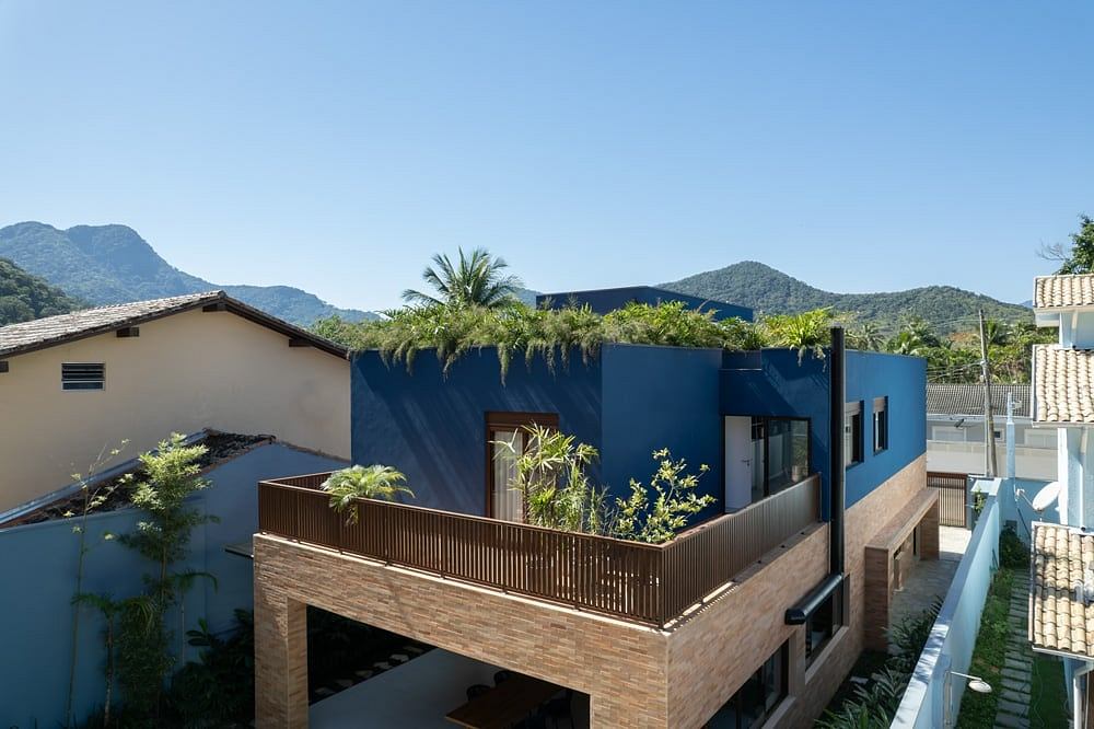 Contemporary tropical-inspired architecture with blue facade, wooden balcony, and lush greenery.
