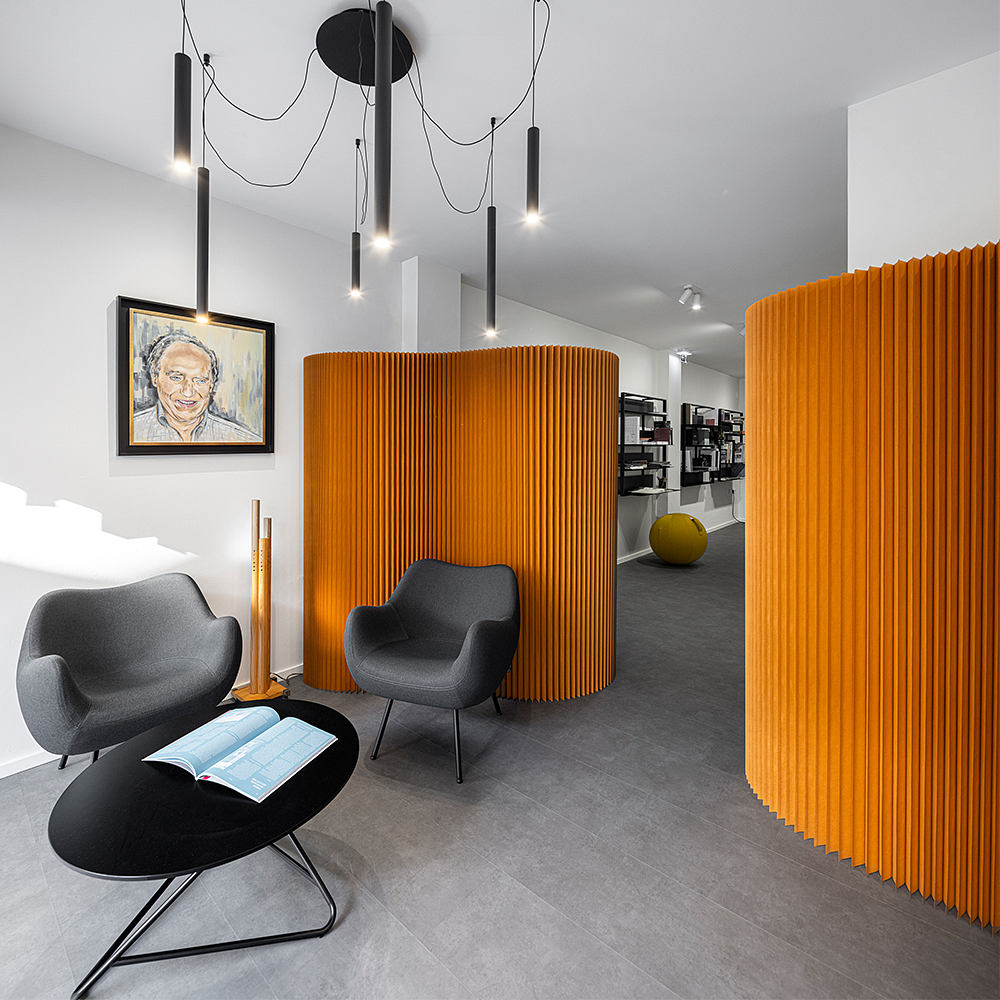 A modern office space with striking orange dividing screens, minimalist furniture, and dramatic lighting.