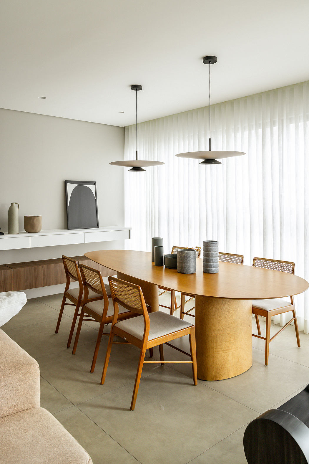 Modern, minimalist dining area with a large wooden table, pendant lights, and built-in shelving.