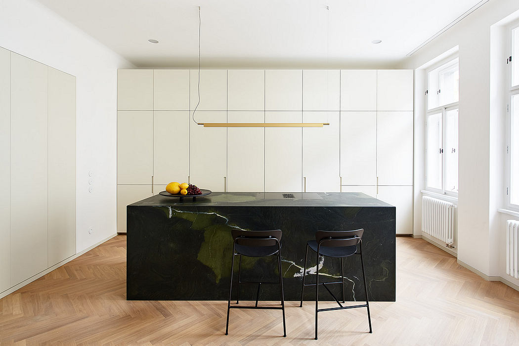 Minimalist kitchen with sleek, dark green marble island and suspended gold light fixture.
