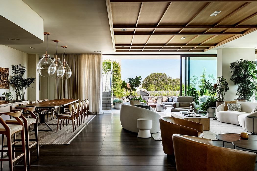 Spacious, modern living area with wooden beamed ceiling, floor-to-ceiling windows, and lush greenery outside.