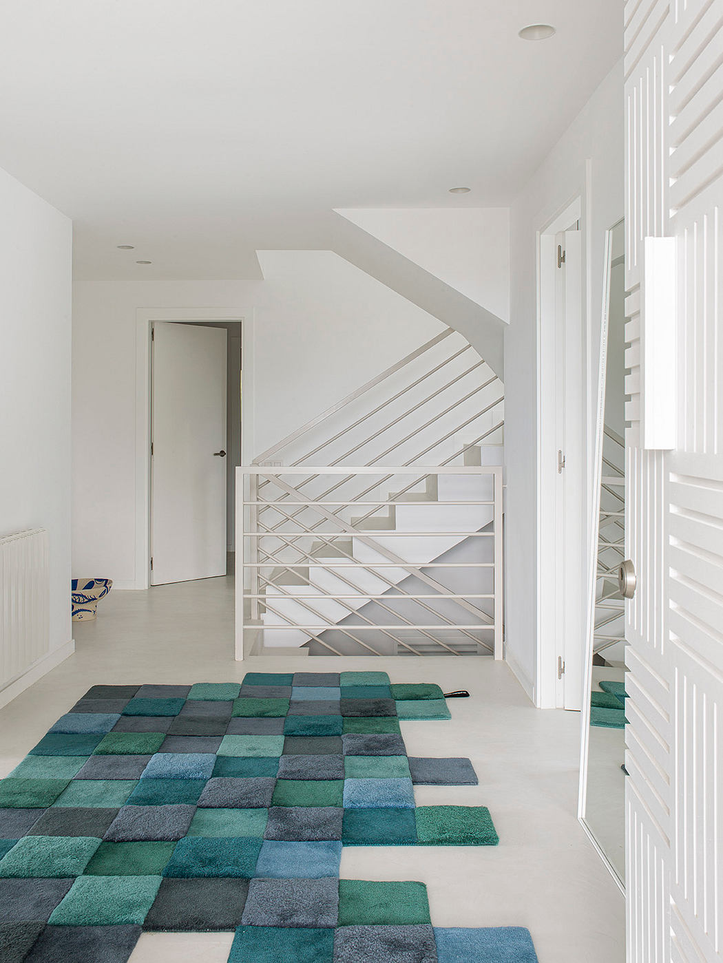 A modern foyer with a geometric staircase and a patterned area rug in teal hues.