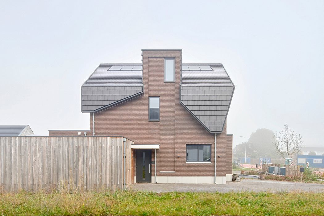 A modern, two-story brick house with gabled roofs, large windows, and a wooden fence.
