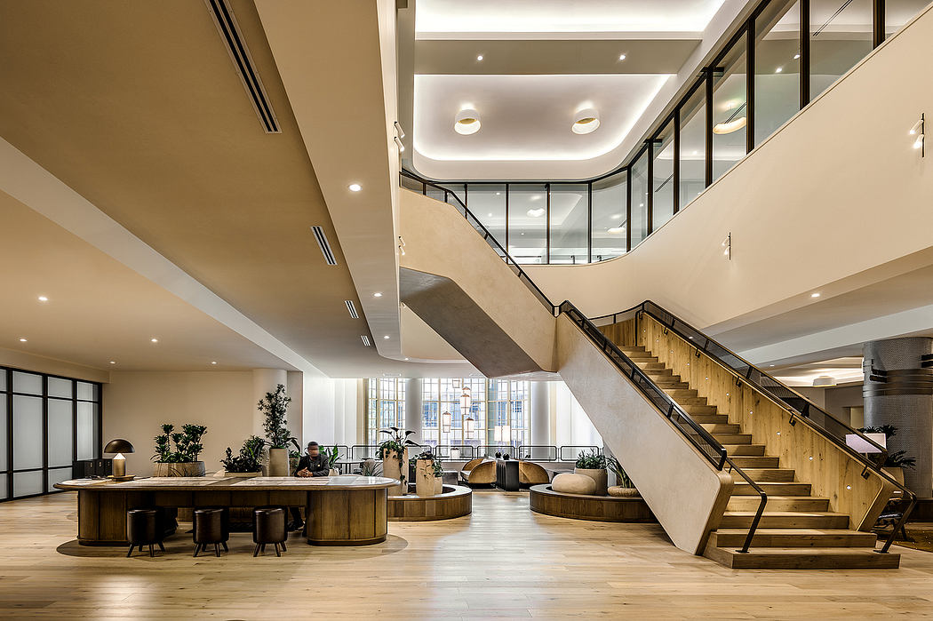 Spacious open-plan lobby with wooden furnishings, glass partitions, and a grand staircase.