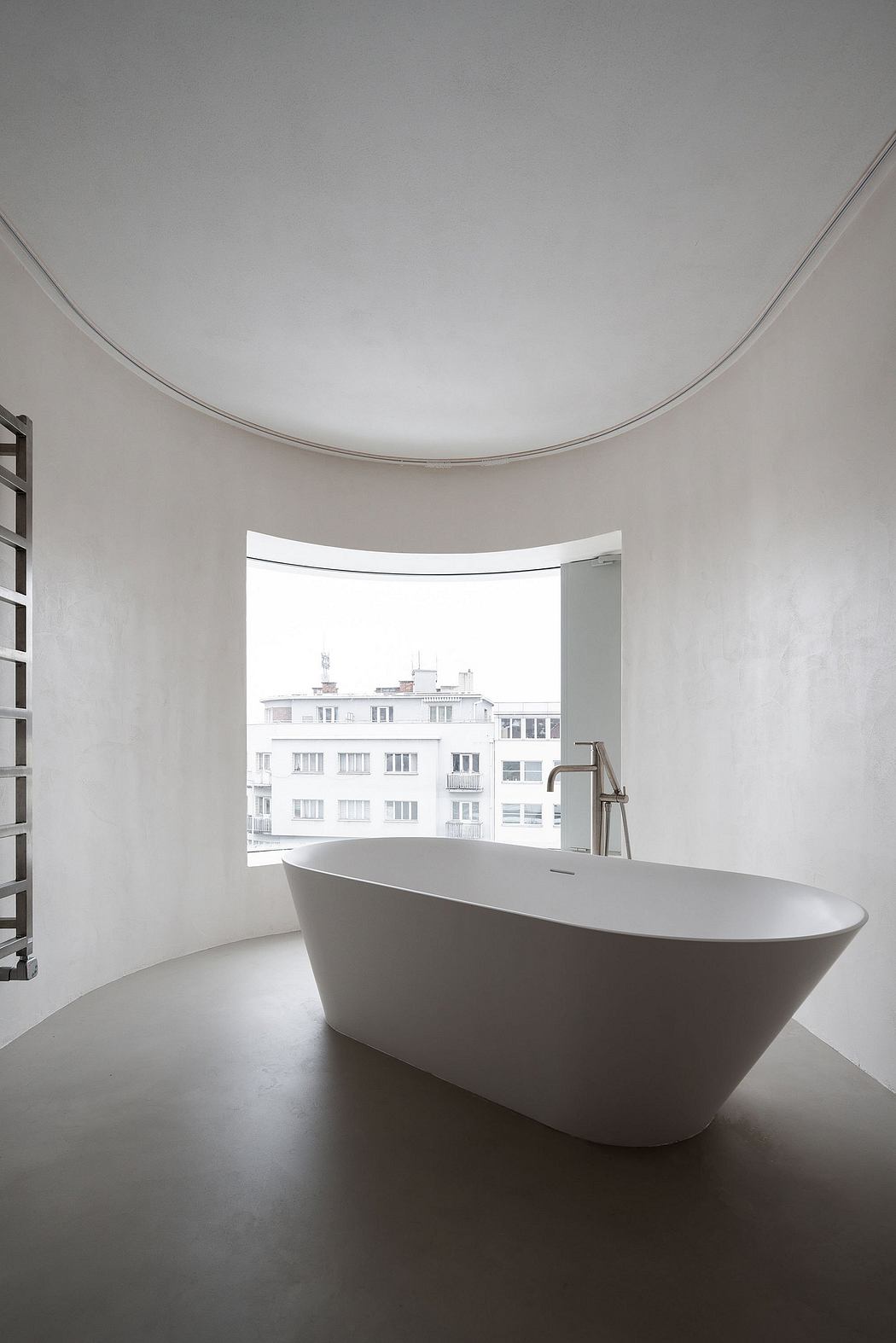 A minimalist bathroom with a large, free-standing bathtub and a curved window overlooking the city skyline.