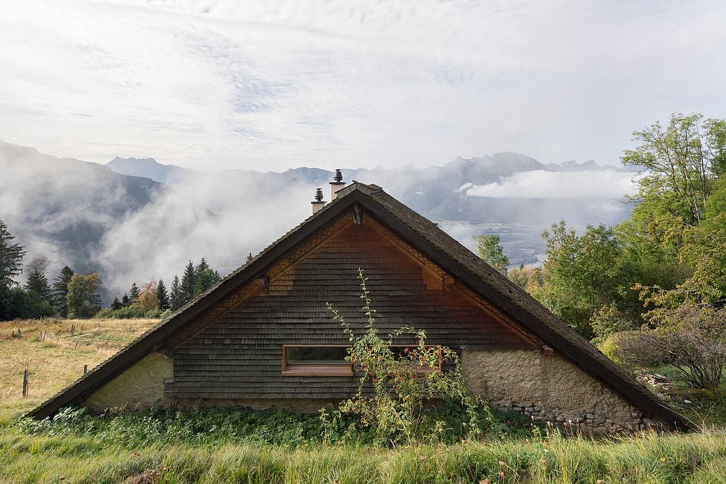 A rustic wooden cabin nestled in a mountainous, misty landscape with a lush garden in the foreground.