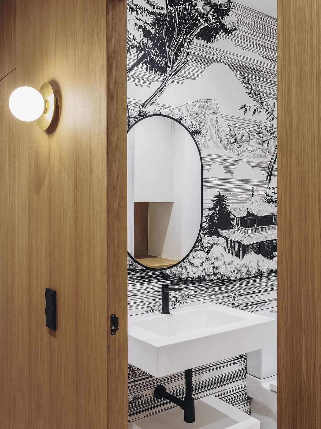 A modern bathroom with a large round mirror, white vanity, and a scenic wallpaper mural.