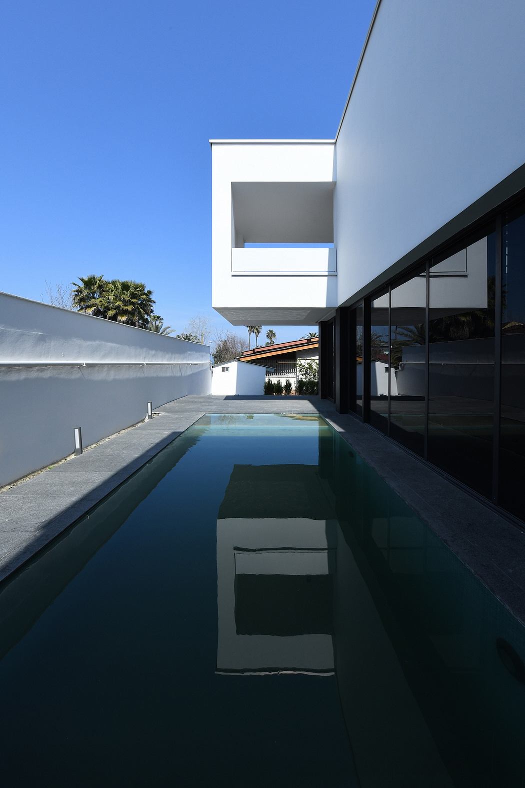 Sleek, modern architecture with a minimalist pool and large windows reflecting the sky.