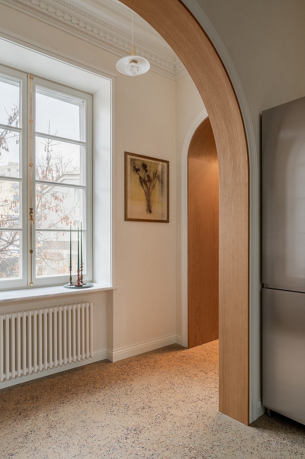 A spacious entryway with an arched wooden doorway, ornate moldings, and a terrazzo floor.