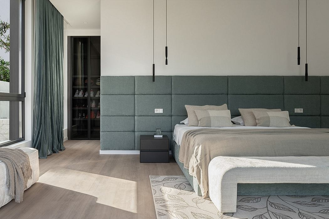 A modern, minimalist bedroom with a luxurious upholstered headboard, pendant lighting, and wood flooring.