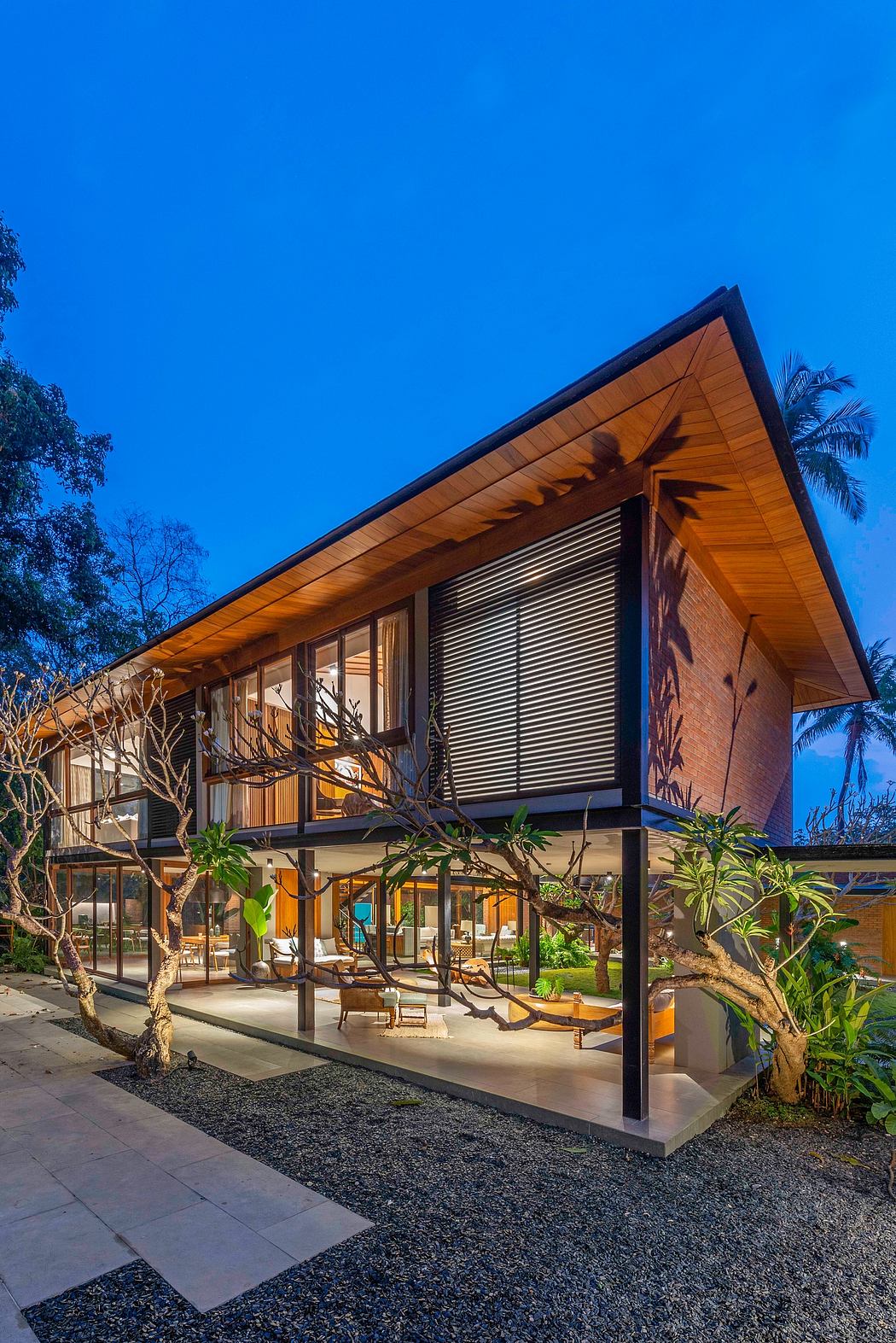 Modern tropical-style villa with wooden roof, large windows, and lush landscaping.